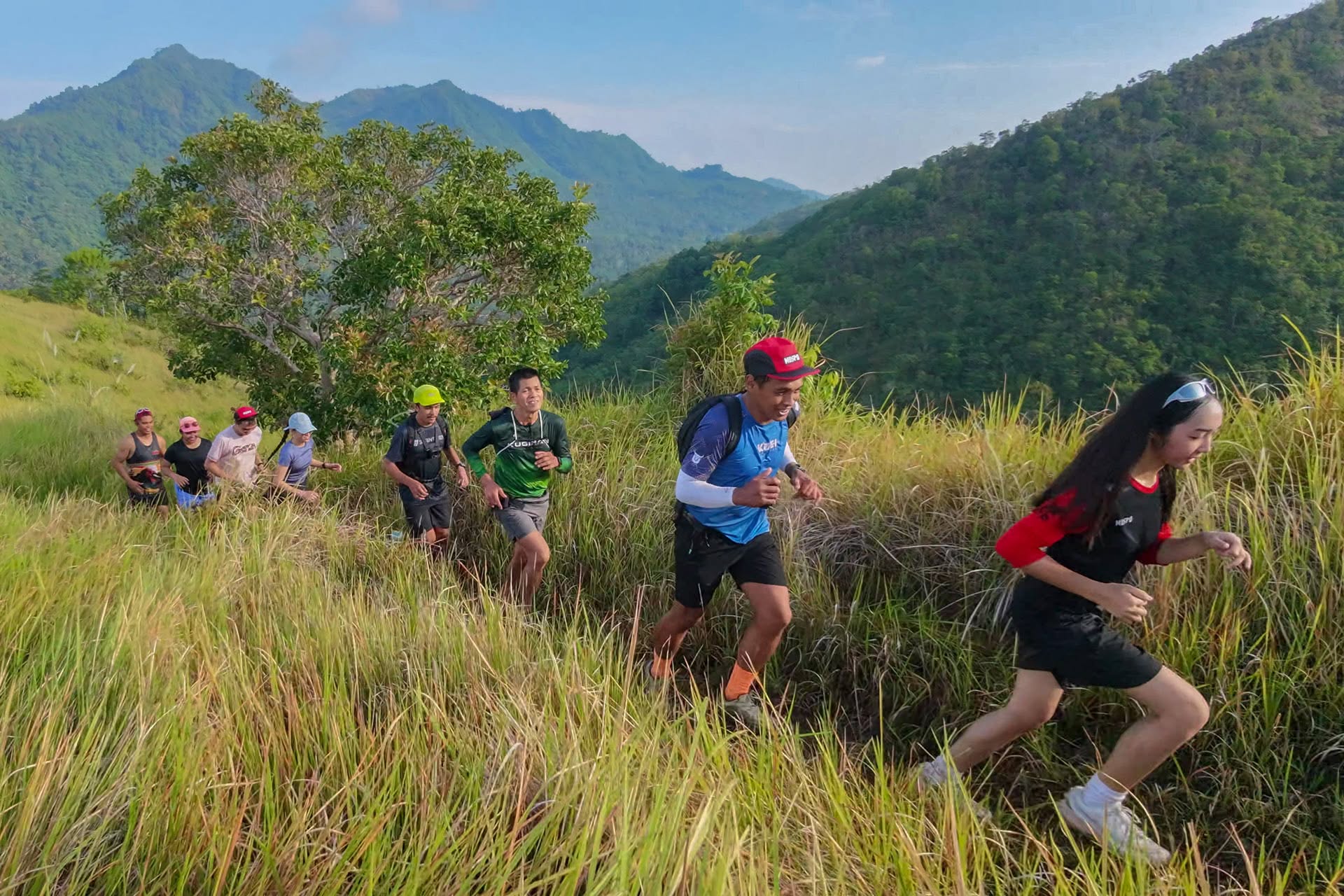 A group of trail runners climbing a grassy ridge with forested mountains behind